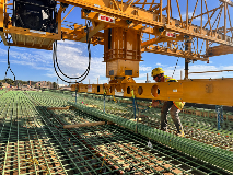 Construction Worker Transporting Rebar Along Bridge