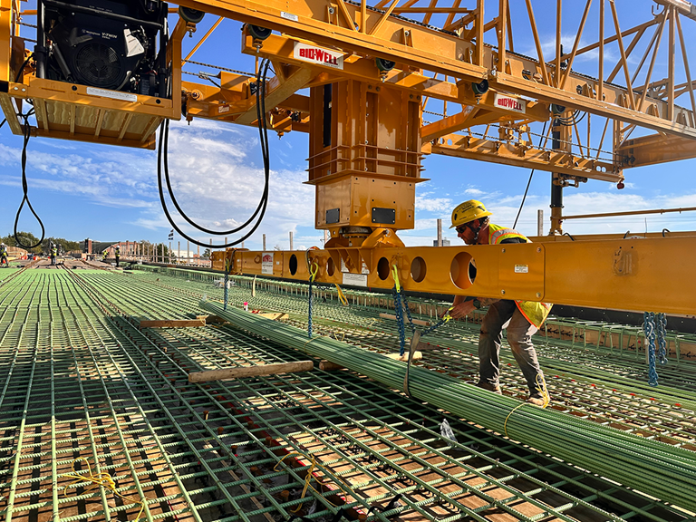Construction Worker Transporting Rebar Along Bridge
